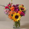 Colorful bouquet of sunflowers, roses, and daisies in a clear glass vase