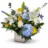 Mixed bouquet with white lilies, blue hydrangeas, and yellow roses in a square vase