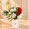 Red roses and white lilies in a white vase with green pompons