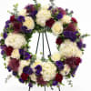 Floral wreath with white hydrangeas, cream roses, and purple blooms on a stand