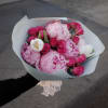 Handheld bouquet of pink peonies and roses wrapped in pale paper
