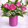 Pink roses arranged in a magenta vase with white filler flowers