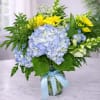 Blue hydrangeas and yellow daisies in a glass vase with a blue ribbon.