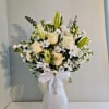 White roses and lilies arranged in a white vase with a ribbon bow