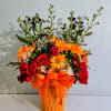 Bouquet of red roses and orange daisies in a glass vase with an orange ribbon