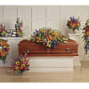 Colorful funeral floral sprays surround a wooden casket in a chapel.