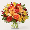 Bouquet of orange roses, lilies, carnations, and yellow alstroemeria in a clear glass vase
