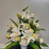 White lilies and cream roses arranged in a vase with fern accents