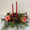Low floral centerpiece with two red taper candles and peach-orange blooms