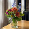 Mixed bouquet in a clear glass vase with orange, purple, and blue flowers