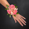 Pink rose wrist corsage with ribbon and pearl accents on a hand