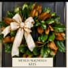 Magnolia wreath with a cream ribbon bow on a dark door