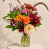 Mixed bouquet of orange, red, and pink flowers in a glass vase