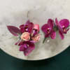 Pair of magenta orchid and peach rose boutonnieres on a round stone surface