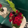 A bold, sculptural composition featuring deep red roses, red gerbera daisies, and