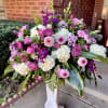 A lush, full-bodied floral arrangement built in a classic white pedestal vase
