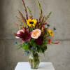 Mixed bouquet in a clear glass vase with sunflowers, roses, and lilies