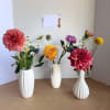 Three small floral arrangements in white vases with colorful blooms
