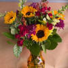 Bouquet of sunflowers, roses, and purple flowers in an amber vase