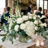 White floral centerpiece in a glass vase with roses, hydrangea, and calla lilies