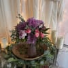 Purple and pink floral arrangement in a mauve vase with candles nearby