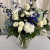 A clear glass vase that showcases clustered white roses, chrysanthemums, pale blue