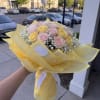Bouquet of pale pink and yellow roses wrapped in yellow paper