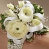 Creamy white ranunculus and roses form a compact, rounded bridal wrist corsage