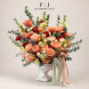 Peach and red rose arrangement in a white pedestal vase with trailing ribbon