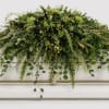 A lush cascade of mixed greenery designed for a funeral or memorial