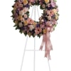 A full, circular sympathy wreath arranged in soft lavender, peach, pink, purple