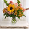 Bouquet of sunflowers, pink roses, and mixed blooms in a clear glass vase