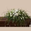 A serene, low-profile casket spray arranged in soft whites and green foliage