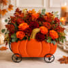 Pumpkin-shaped floral arrangement with orange and red blooms in a black metal cart.