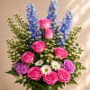 Bouquet of pink roses, blue delphinium, and white daisies in a vase