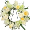 White floral wreath with pale yellow roses on a black stand