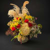 Mixed bouquet with red roses, yellow blooms, and tall dried grasses in a low vase