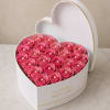 Densely packed pink roses artfully arranged in a white heart-shaped box create