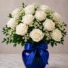 White roses arranged in a blue glass vase with a ribbon