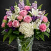 Pink roses, white lilies, and purple flowers in a clear glass vase