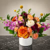 Mixed bouquet of roses, carnations, and purple blooms in a white vase