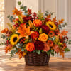 Autumn flower arrangement in a wicker basket with roses, lilies, and sunflowers