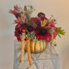 Deep red floral arrangement in a gold pumpkin-shaped vase with trailing blooms