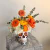Orange and yellow flowers arranged in a decorated skull vase