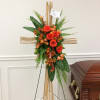 Orange rose funeral spray on a bamboo cross stand beside a casket