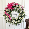 White daisy wreath with a bright pink ribbon on a black stand