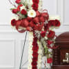 Cross-shaped floral tribute with red roses, white flowers, and a large red ribbon
