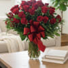 Red roses arranged in a clear glass vase with a red ribbon bow