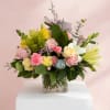 Mixed bouquet of pink, yellow, and white flowers in a clear square vase
