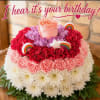 Round floral cake with pink, red, and white blooms and birthday topper